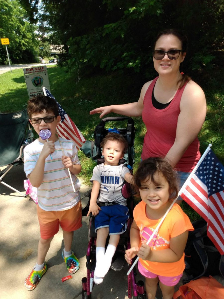 Isaac sits in his stroller with mom, Traci, next to him, and siblings, Haddon and Noel smiling nearby.