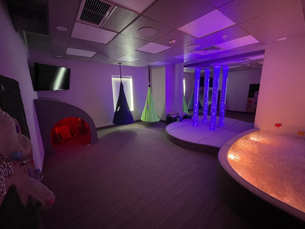 Darker room with light up ball pit, light up bubble tubes, and swings.