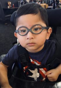 Little boy with dark hair and glasses sits.