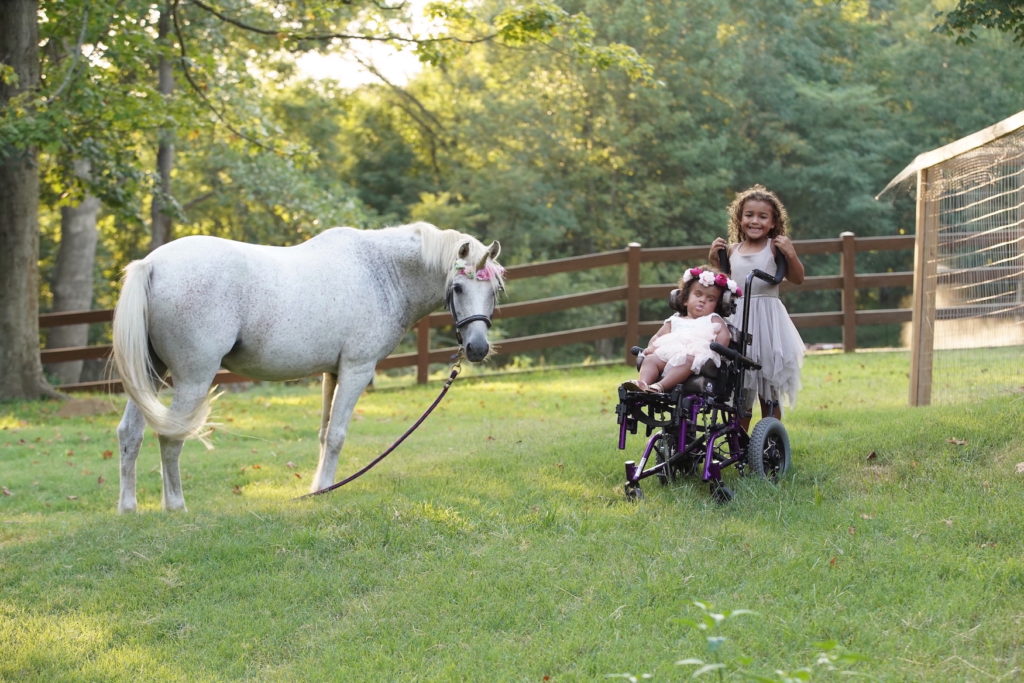 Tala and her sister KaiLayna in a field with a horse wearing a unicorn horn. The girls are dressed in princess outfits.
