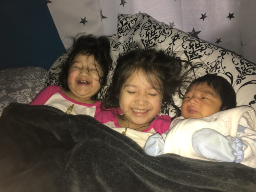 Infant Odin laying next to his sisters in a bed