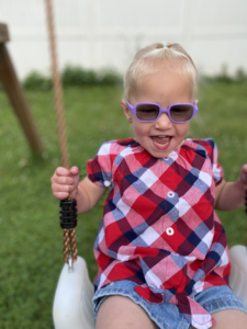 Little girl on a swing with sunglasses on and is smiling.