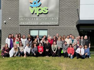 A group of VIPS team members stand and sit in front of the VIPS building in Indianapolis.