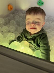 Child is standing in a ball pit that is lit up and he is smiling.