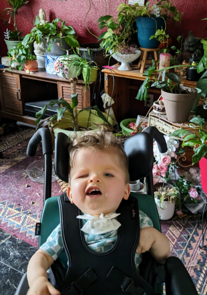 Young boy surrounded by plants in his wheelchair smiling