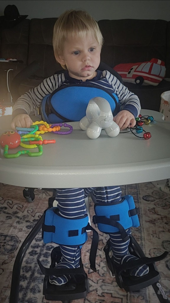 Boy is in an adaptive stander with toys in front of him