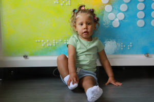 A toddler sits in front of a colorful sign made out of glass.