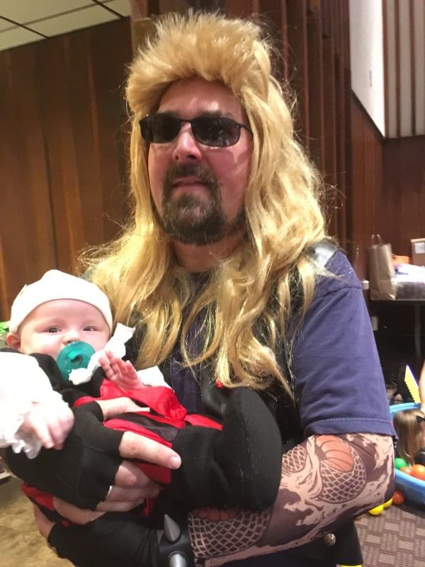 A man with a wig and sunglasses holds a baby