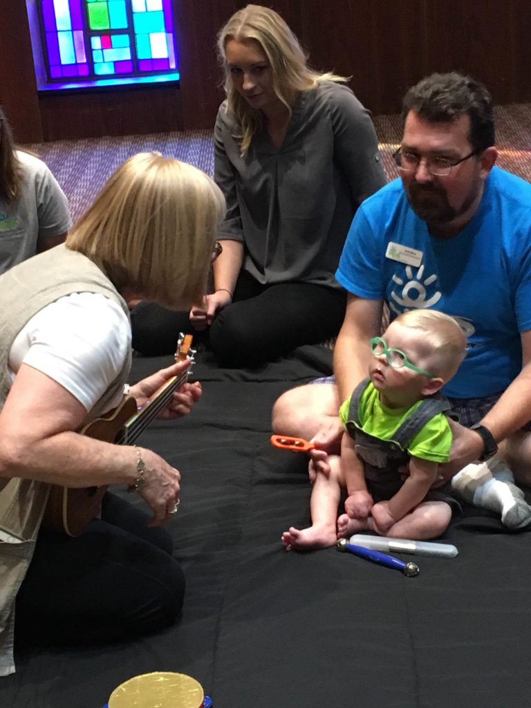 A woman with light hair is signing to a toddler being held by a man