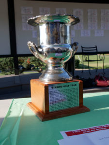 The Yum! Golf Tournament winners trophy. It's a silver cup in a wood base. There is a silve metal plate engraved with the names of past year winners.
