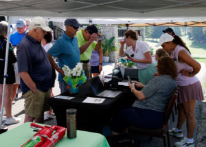 VIPS staff sitting at a table signing in golfers. Golfers are standing on the other side wait to register.