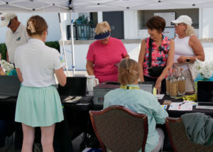 VIPS staff sitting at a table signing in golfers. Golfers are standing on the other side wait to register.