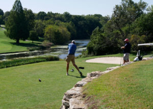 Two male golfers, one teeing off while other watches.