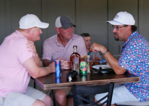 Doug Voss chats with two of his teammates sitting at at table in the clubhouse after the scramble.