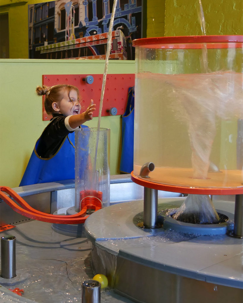 A smiling girl is about to stick her hand in a water jet that's part of a display at the Kentucky Science Center.