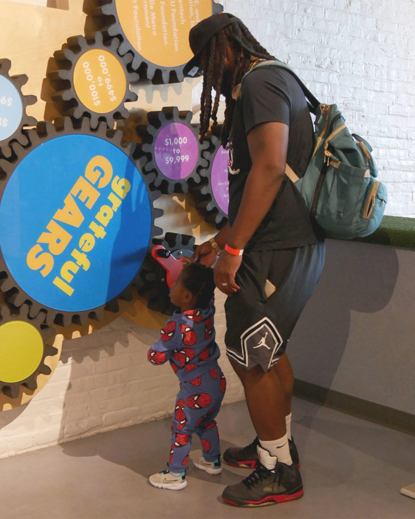 With a bit of help from his father, a small boy wearing Spiderman PJs turns the giant gears on the wall at the Kentucky Science Center.
