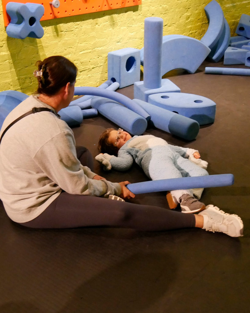 A boy lies on the floor playing with pool noodles with his mother by his side at the Kentucky Science Center.