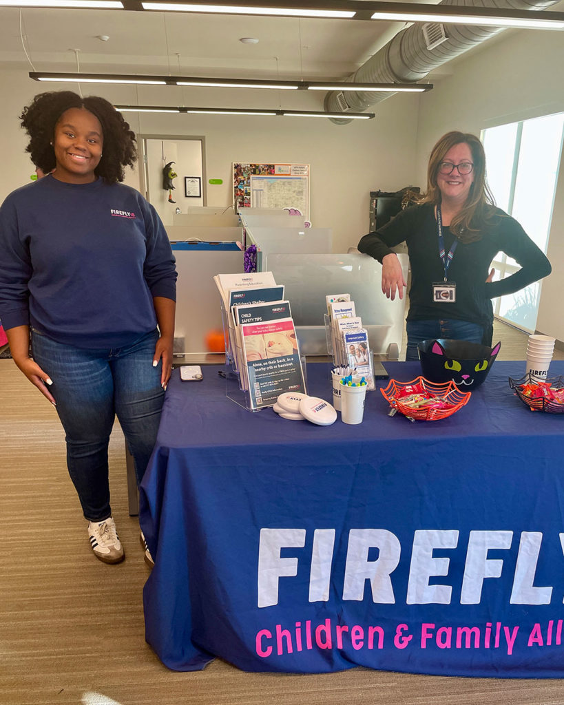 Two women representing Firefly pose for a photo behind their display table at the FRC.