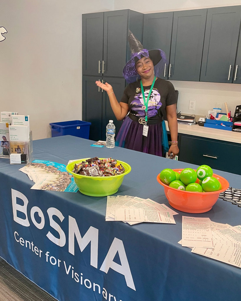 A woman representing Bosma wears a witch's hat and poses for a photo behind their table at the FRC.