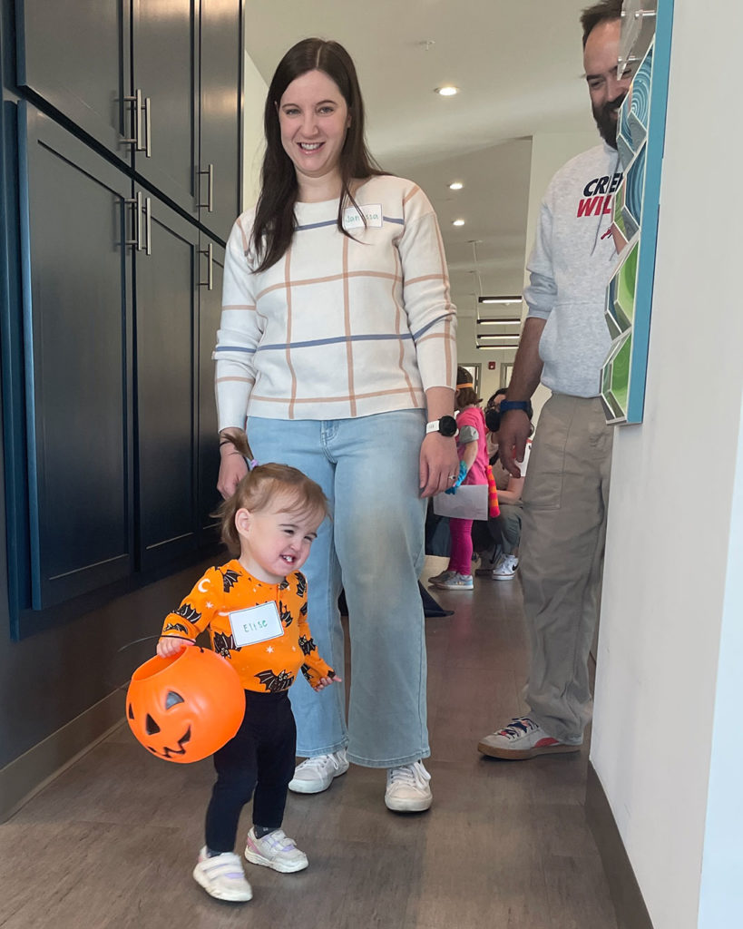 A small girl with her parents smiling while holding a Jack O'Lantern.