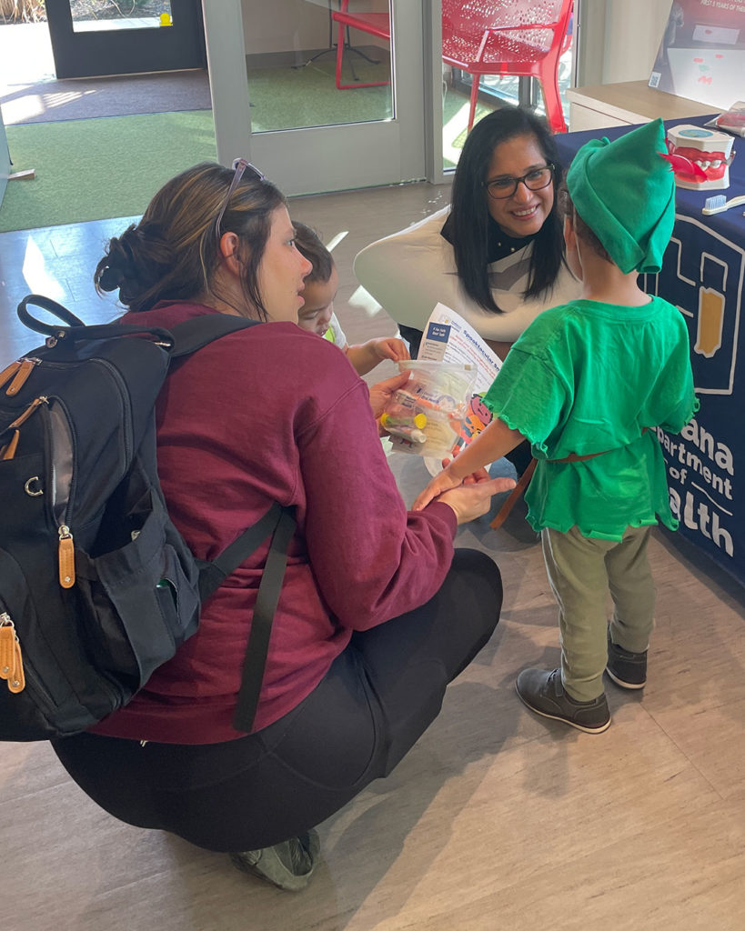 A small boy in an elf costume talks to the woman from the Oral Health Division of the Indiana Department of Health.