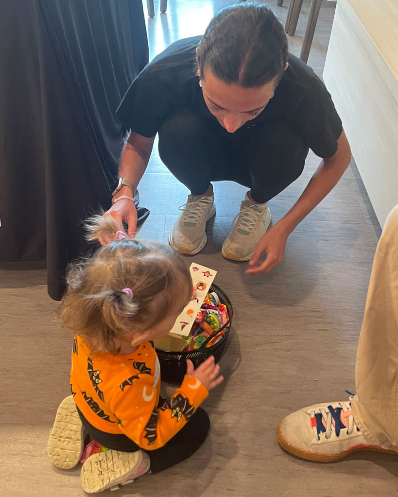 A small girl chooses a sticker sheet from a basket of toys while a woman from the Indiana Blind Children's Foundation helps.