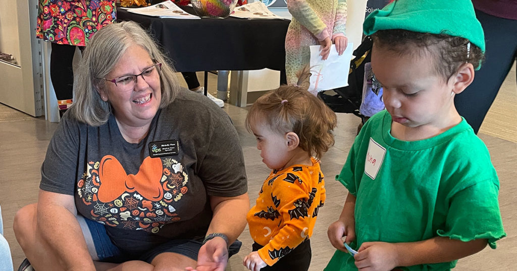 Michelle Flora sits on the floor, talking to a small girl.