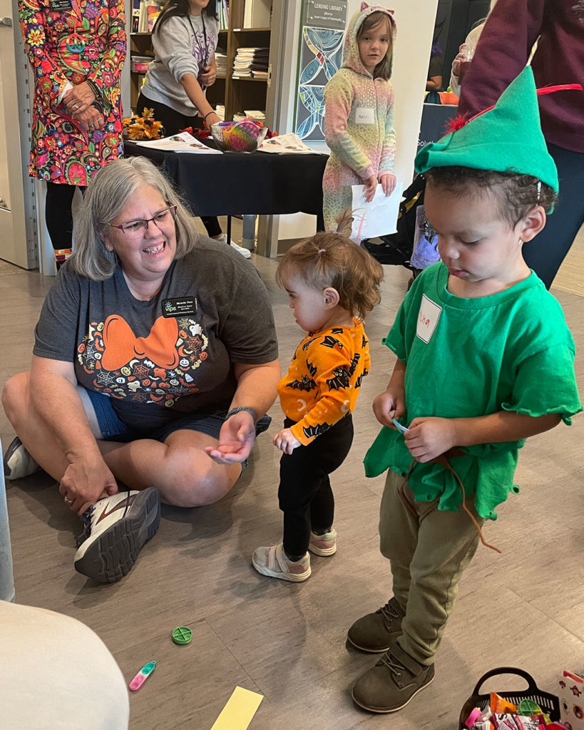 Michelle Flora sits on the floor, talking to a small girl.