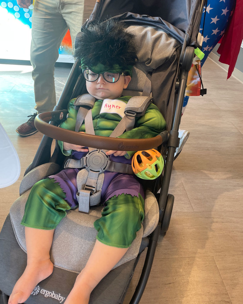 A small boy wearing a Hulk costume sits in his stroller.