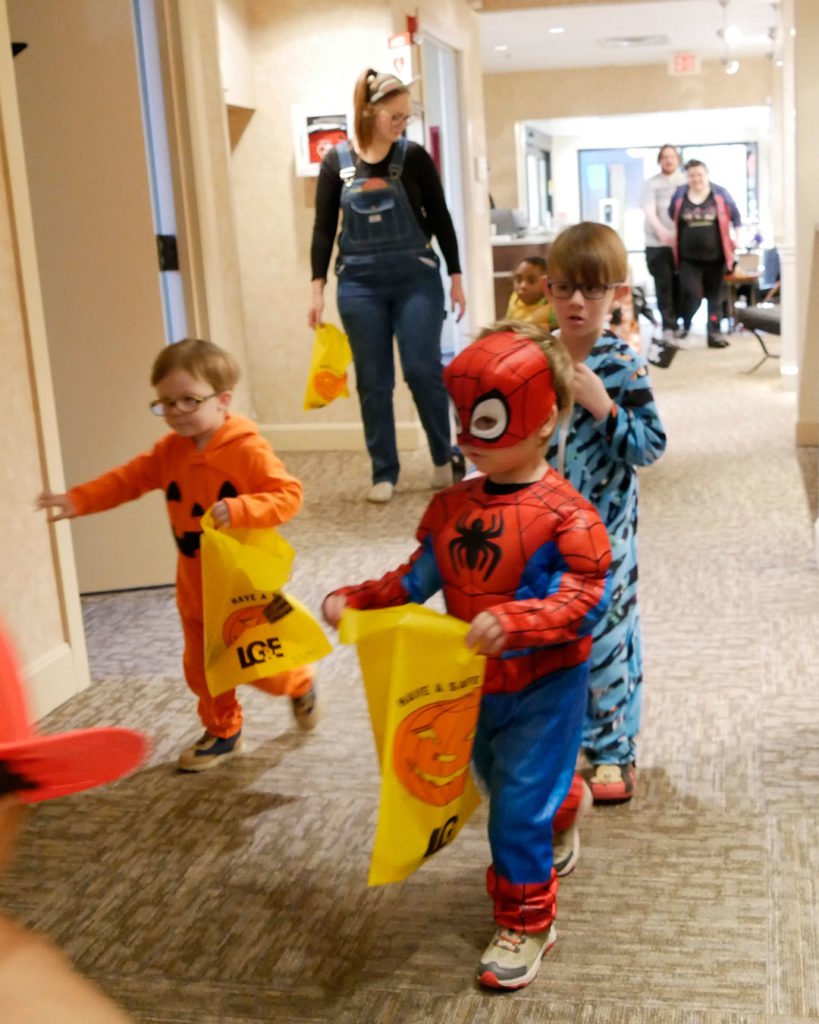 Spiderman, a pumpkin, and a blue tiger head down the hallway to the next treat station.