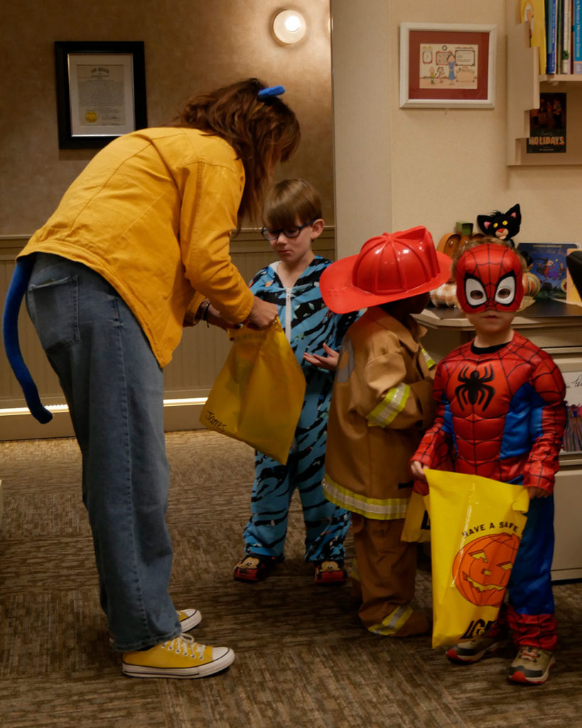 Miss Laney helps a blue tiger, a fireman, and Spiderman with the treat bags.