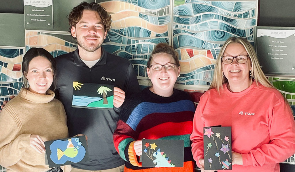 Four volunteers from TWG pose for a photo while holding the birthday cards they made.
