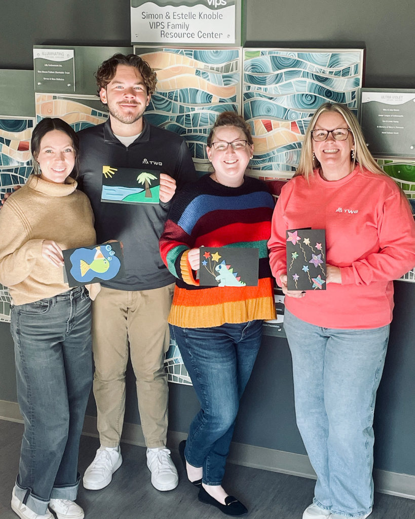 Four volunteers from TWG pose for a photo while holding the birthday cards they made.