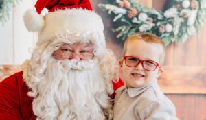 Clyde is smiling and wearing his new, red glasses while sitting on Santa's lap.