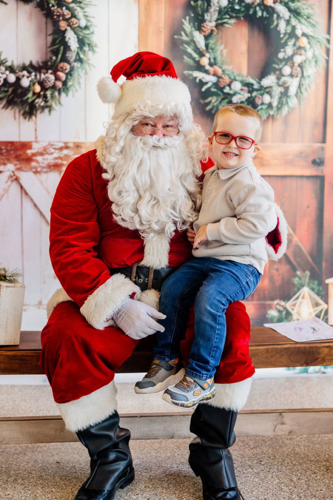 Clyde is smiling and wearing his new, red glasses while sitting on Santa's lap.