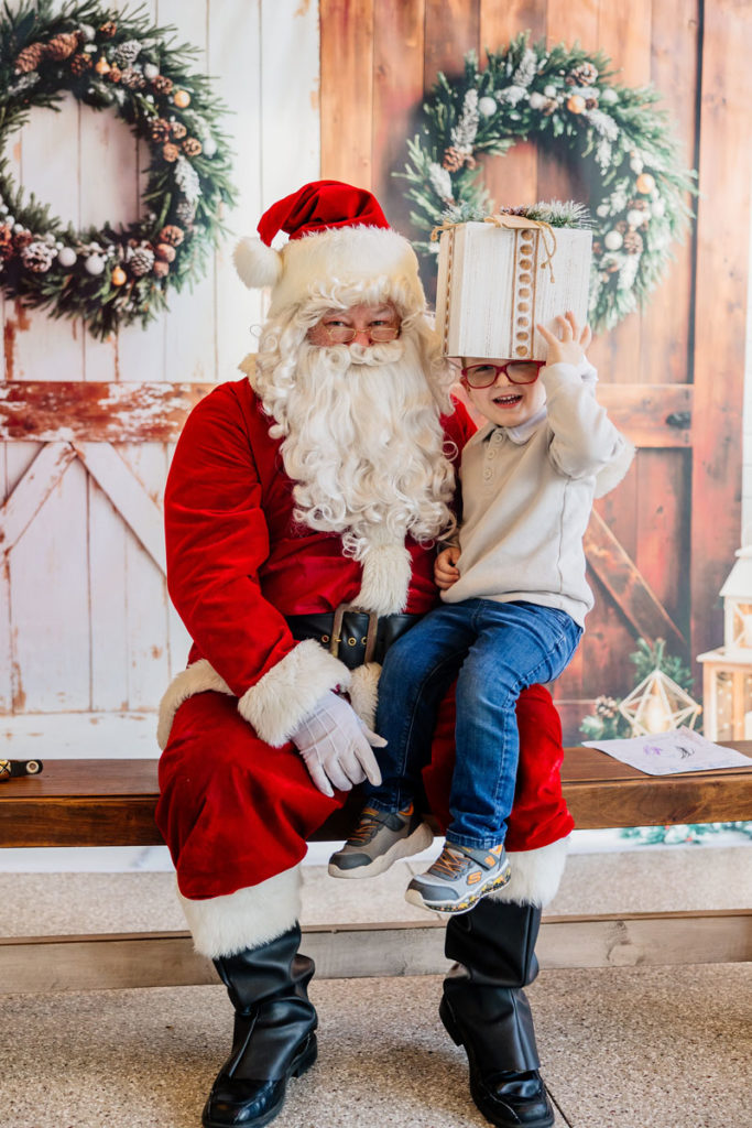Clyde is laughing and putting an empty gift box over his head while sitting on Santa's lap.