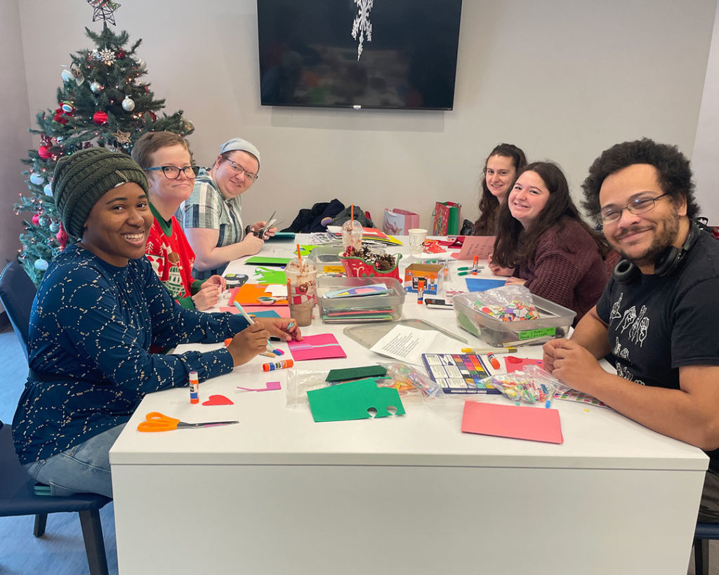 Six volunteers sit at a large table in the FRC and make welcome cards.