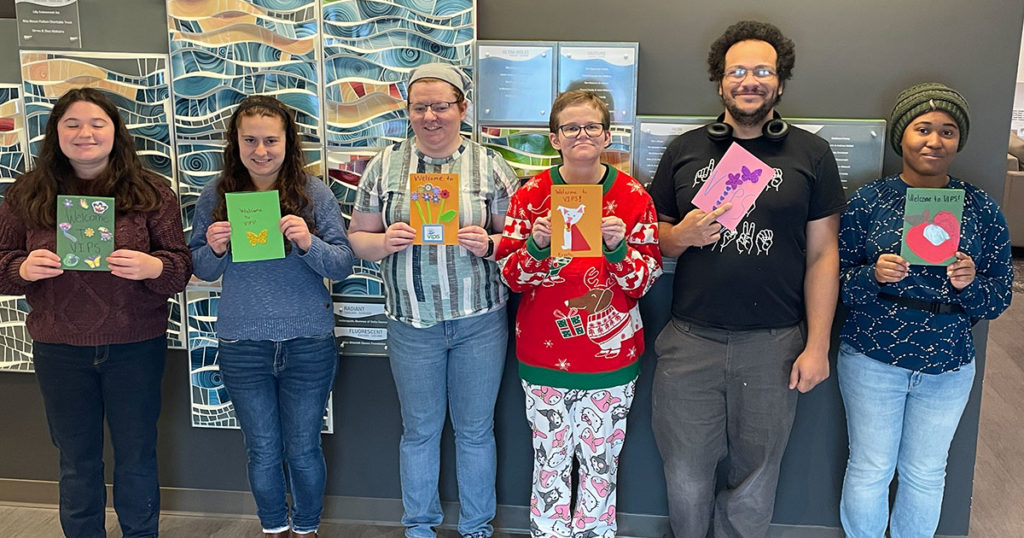 Six volunteers pose for a photo in the FRC while holding some of the welcome cards they made.