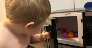 Phoenix sits on the floor and is placing multicolored plastic balls in his microwave.