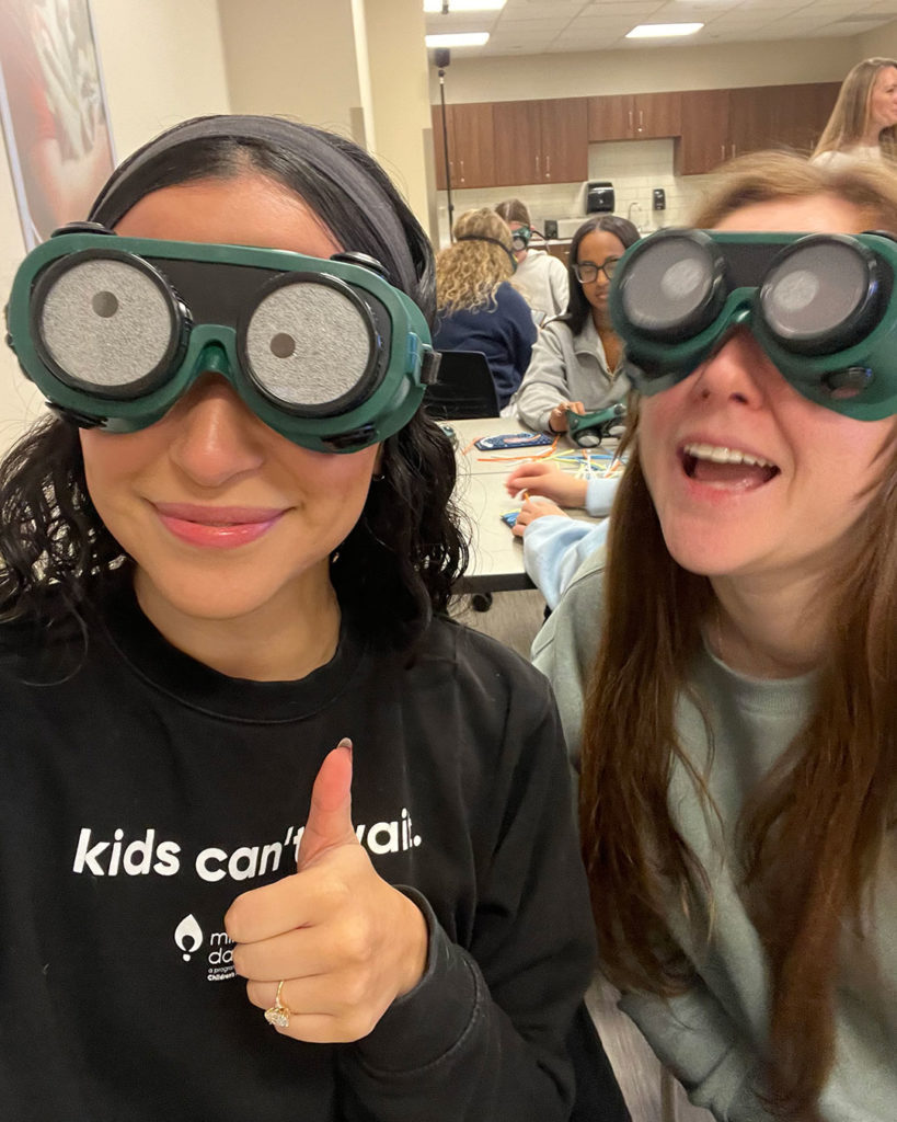 Two female OT students take a selfie while wearing simulation goggles.