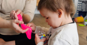 Penelope sits in the floor and exams a slime jar.