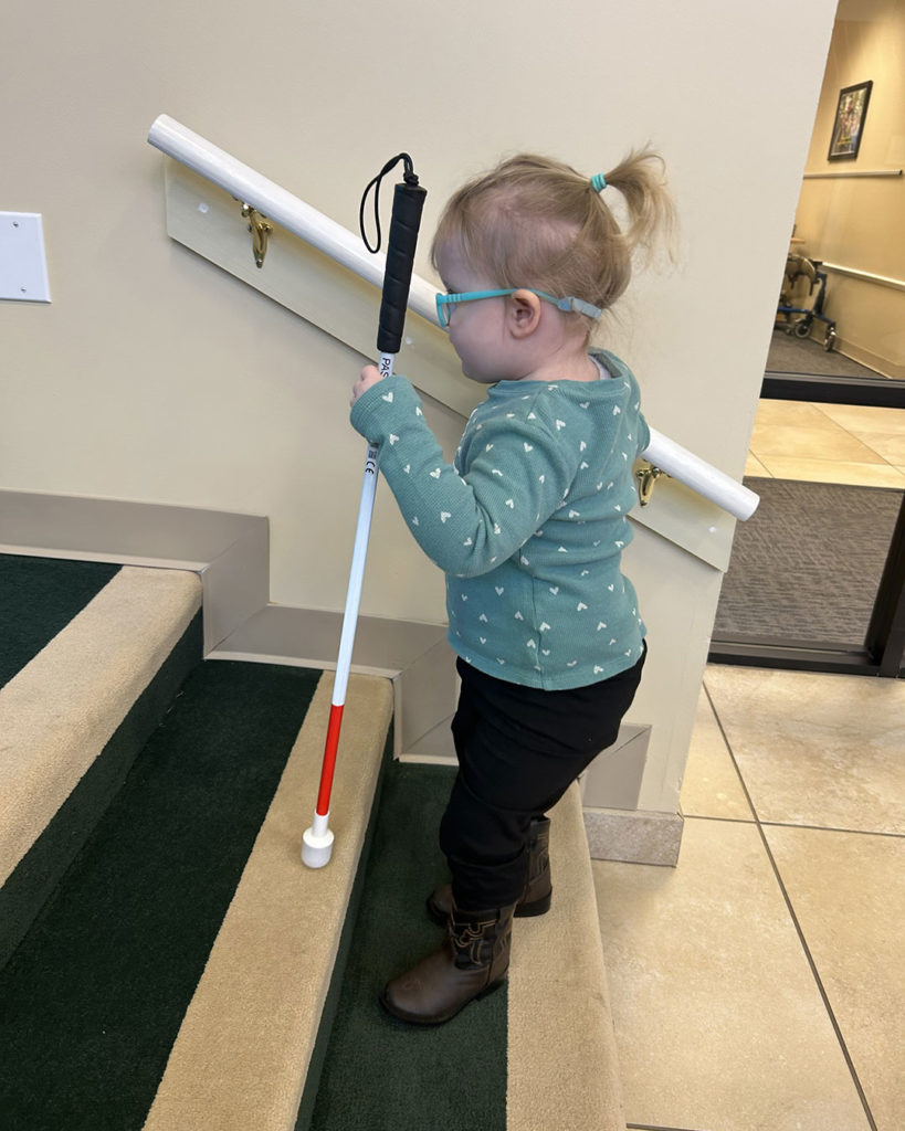 Roxanne is climbing the steps in Kids Town using her white cane.