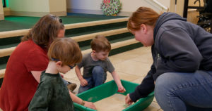 Ranger Erin and Ms. Staci play in a sandbox with two small boys.