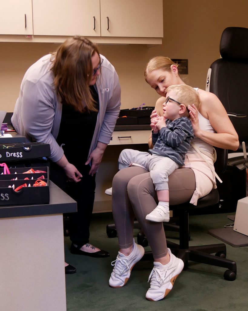 Megan checks the frame fit on a small boy as he sits in his mother's lap.