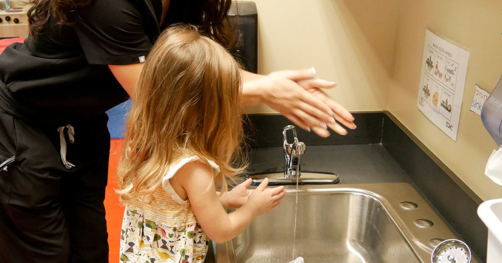 A small girl washes her hands while a female physician assistant student demonstrates.
