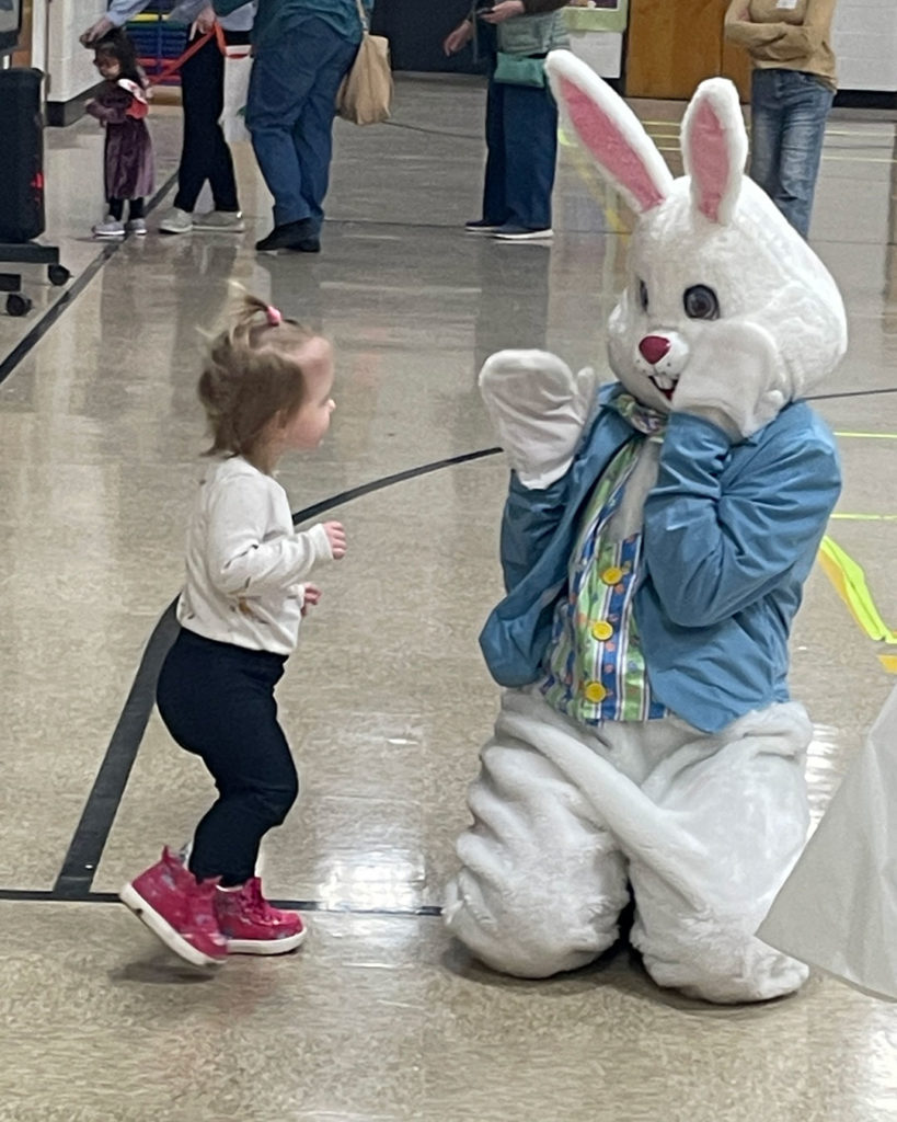 A small girl runs up to the Easter Bunny to say hello.