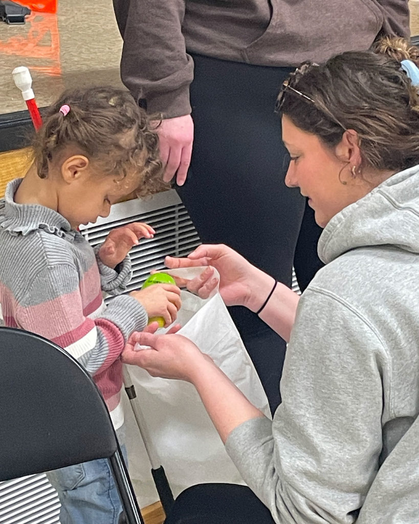 A volunteer helps a small girl place her Easter egg in her bag.