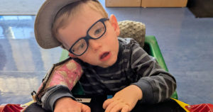 Wells is sitting at his desk using blocks on a board that says Home and School.