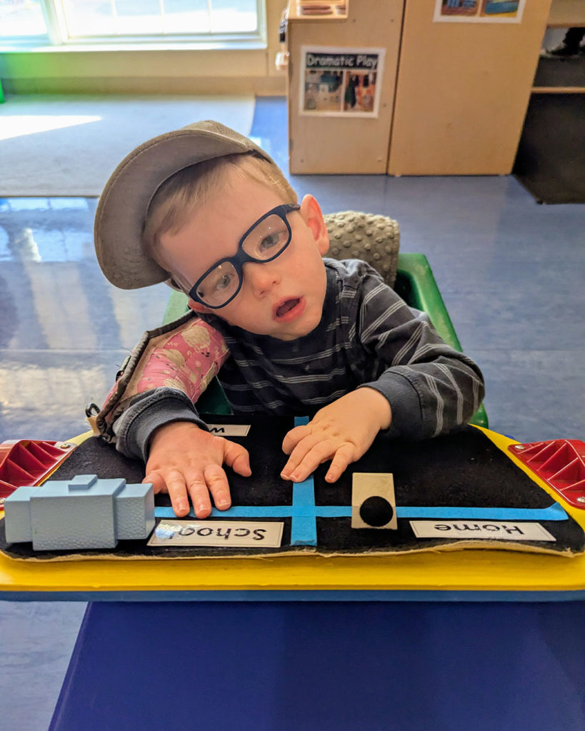 Wells is sitting at his desk using blocks on a board that says Home and School.