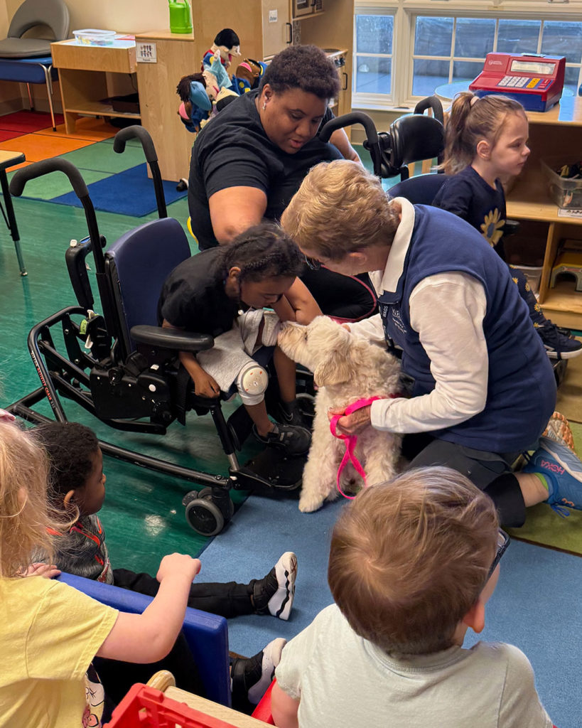 Ms. Lana from W.A.G.S. introduces a small boy to Bella the Therapy Dog during a classroom visit.